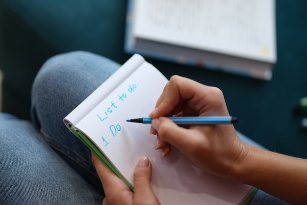 Femme Assise Sur Un Canapé Et écrivant Un Journal Pour Faire La Liste Pour Aujourd'hui En Gros Plan