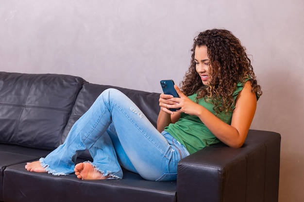 Femme assise sur le canapé en écrivant un SMS sur son téléphone portable.