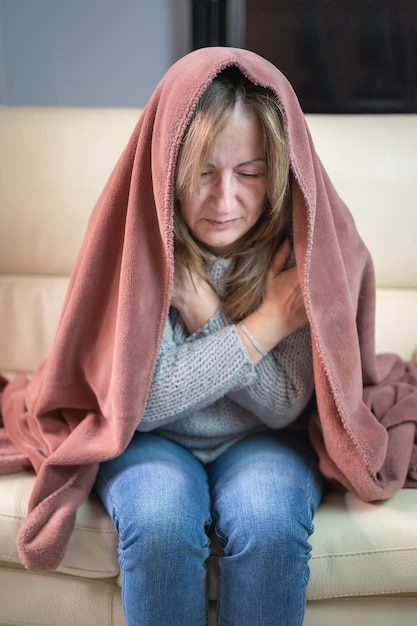 Femme assise sur un canapé et enveloppée dans une couverture froide pendant l'hiver et économies d'énergie