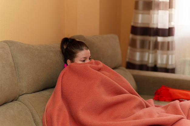 Femme assise sur le canapé enveloppée dans une couverture sans chauffage