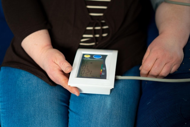 Femme assise sur le canapé et mesurant sa tension artérielle