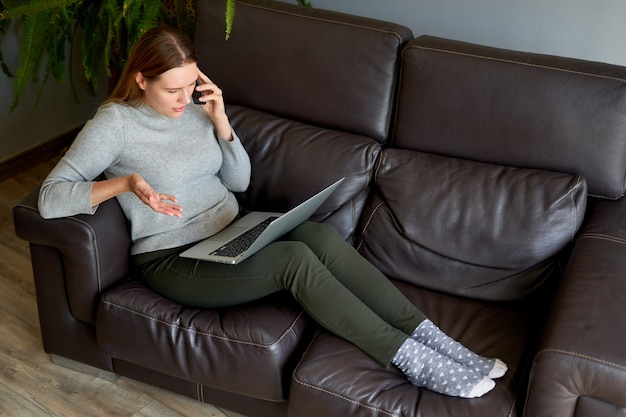 Femme assise sur un canapé avec ordinateur portable et parler au téléphone à la maison. Étudiant étudiant sur ordinateur portable et utilisant le téléphone.