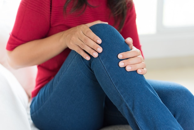 Photo femme assise sur le canapé et le sentiment de douleur au genou, soins de santé et concept médical.