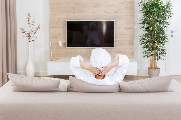 Femme assise sur un canapé avec une serviette sur la tête devant la télé