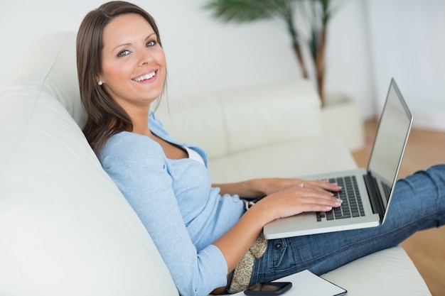 Femme assise sur le canapé avec son ordinateur portable