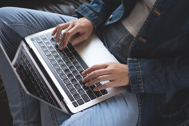 Femme assise sur un canapé en tapant sur un ordinateur portable à la maison