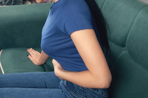 Femme assise sur le canapé tient son estomac dans la douleur