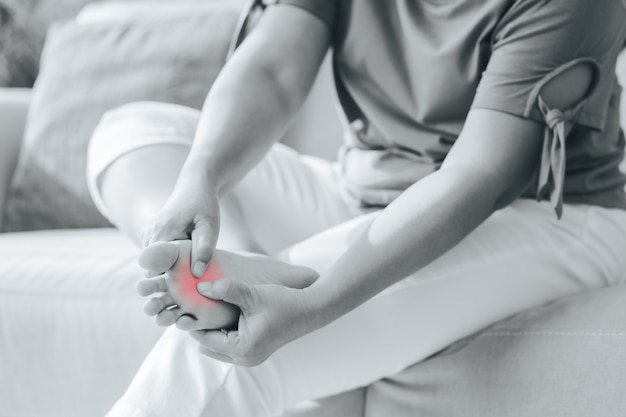 Femme assise sur le canapé et tient son pied souffrant de douleurs au pied avec surbrillance rouge