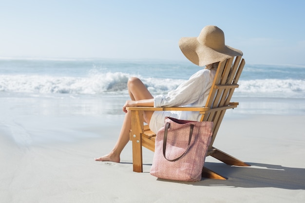Femme assise sur une chaise longue en bois au bord de la mer