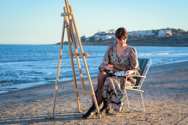 Une femme assise à un chevalet peignant au bord de la mer