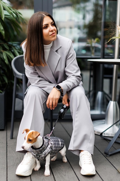 Femme assise avec un chien Jack Russell Terrier habillé en costume pour chiens à l'extérieur dans un café