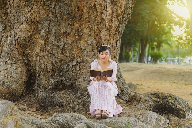 Femme assise à côté d'un tronc d'arbre dans un parc lisant un livre Journée mondiale du livre Concept de la lecture