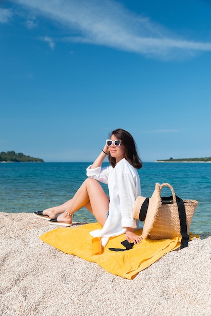 Femme assise sur une couverture jaune à la plage de la mer en tenue d'été