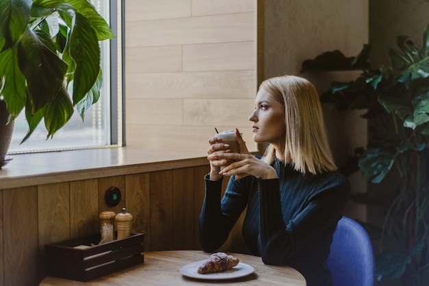 femme assise dans un café le matin avec café et croissant