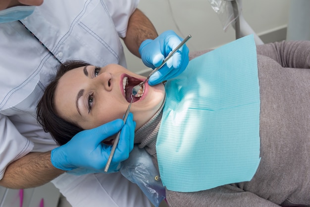 Femme assise dans une chaise de dentiste, médecin examinant les dents