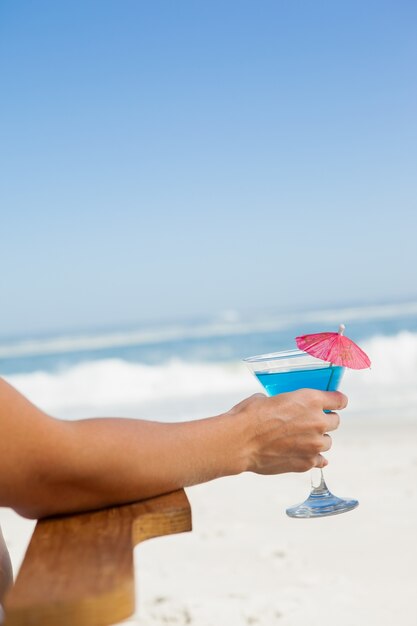 Femme assise dans une chaise longue avec un cocktail à la plage