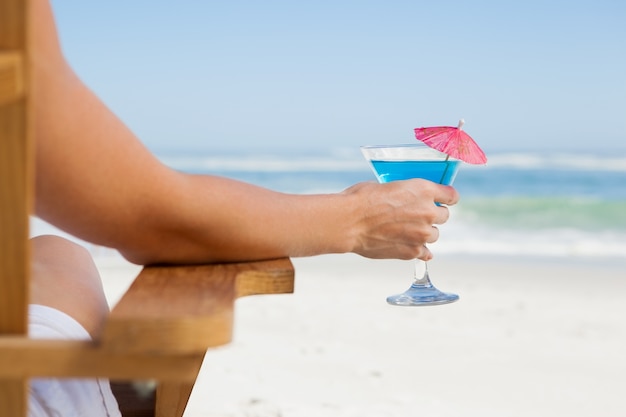Femme assise dans une chaise longue avec un cocktail à la plage