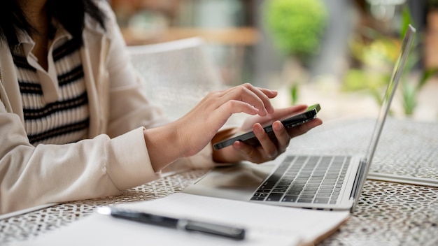 Une femme assise dans un espace extérieur et utilisant son téléphone tout en travaillant à distance depuis un café