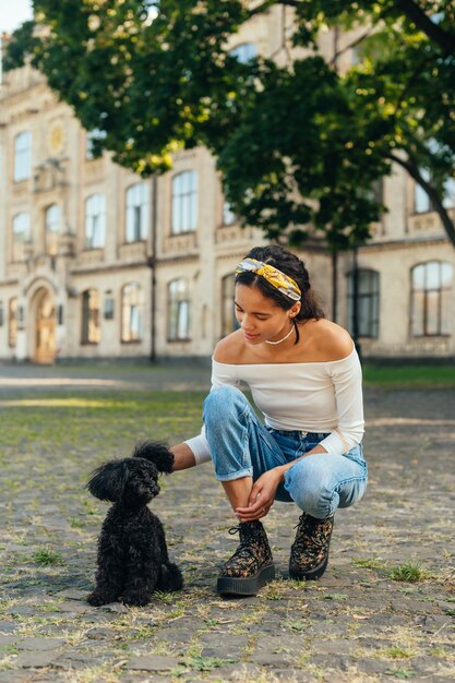 Femme assise dans la rue et jouant avec un petit chien noir Caniche toy de race de chien