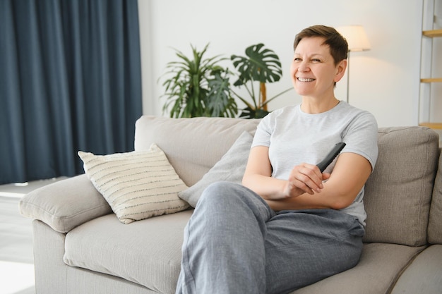 Femme assise dans le salon tenant la télécommande en souriant