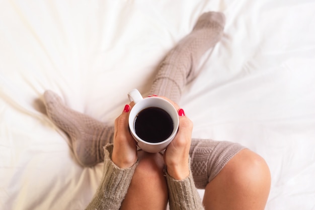 Femme assise dans son lit en buvant une tasse de café