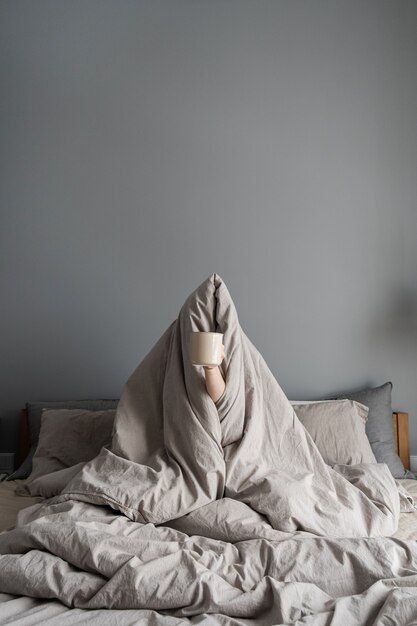 Femme assise dans son lit, tenant une tasse de café à la main