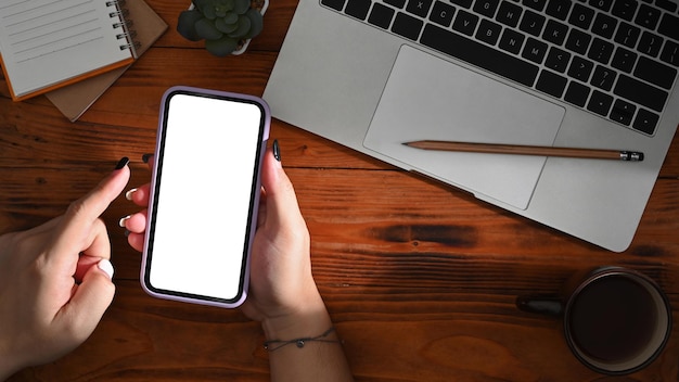 Femme assise devant un ordinateur portable et tapant un message sur un téléphone intelligent