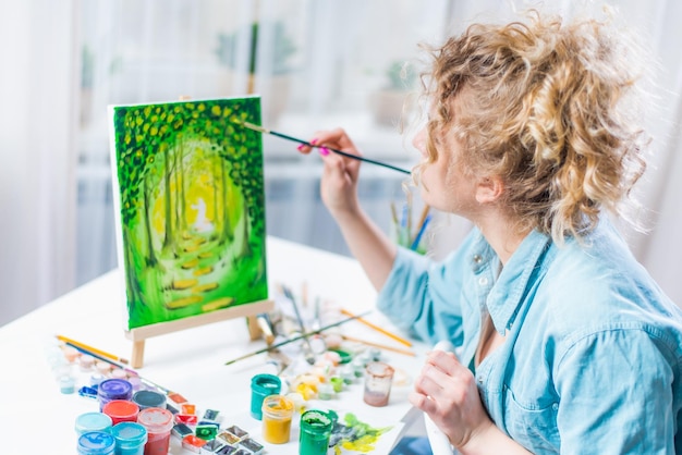 Femme assise devant un tableau et peinture au pinceau sur toile à la maison
