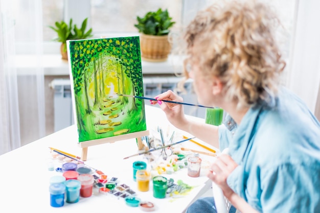 Femme assise devant un tableau et peinture au pinceau sur toile à la maison