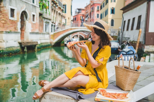 Femme assise sur un étang avec vue sur le canal de Venise en train de manger de la pizza