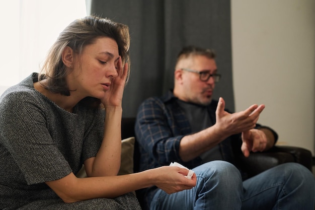 Une femme assise avec une expression triste pendant qu'un homme parle en faisant des gestes