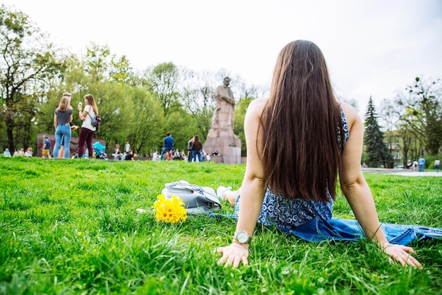 Femme assise sur l'herbe dans le parc de la ville avec des fleurs jaunes. vue de derrière