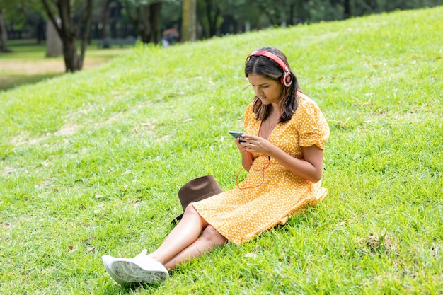 Femme Assise Sur L'herbe écoutant De La Musique Avec Des écouteurs Tout En Envoyant Des Sms Avec Son Téléphone Portable