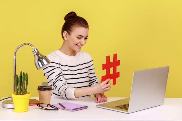 Femme assise sur le lieu de travail montrant un grand symbole de hashtag rouge sur l'écran d'un ordinateur portable partageant du contenu viral