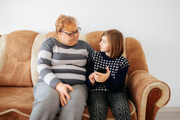 Une femme assise à la maison avec son enfant en utilisant un smartphone pour lui apprendre de nouvelles choses petits-enfants assis