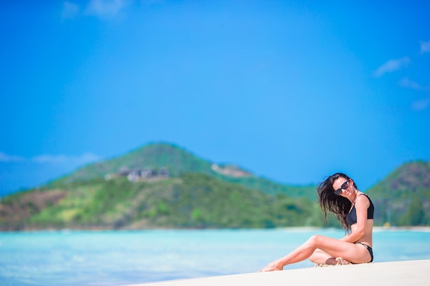 Femme assise sur la plage en riant et en profitant des vacances d'été en regardant la caméra. Beau modèle en bikini assis.