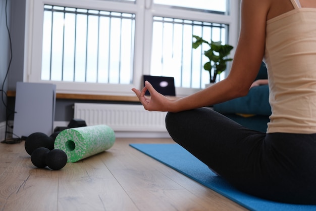 Femme assise en position du lotus sur un tapis bleu à la maison