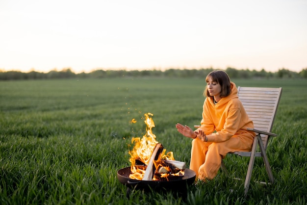 Femme assise près de la cheminée sur un champ vert au coucher du soleil