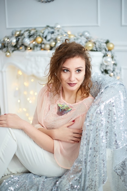 Femme assise près d'une cheminée dans un salon décoré. Intérieur élégant du Nouvel An avec sapin de Noël, cheminée blanche, cadeaux et décorations. Fêter Noël