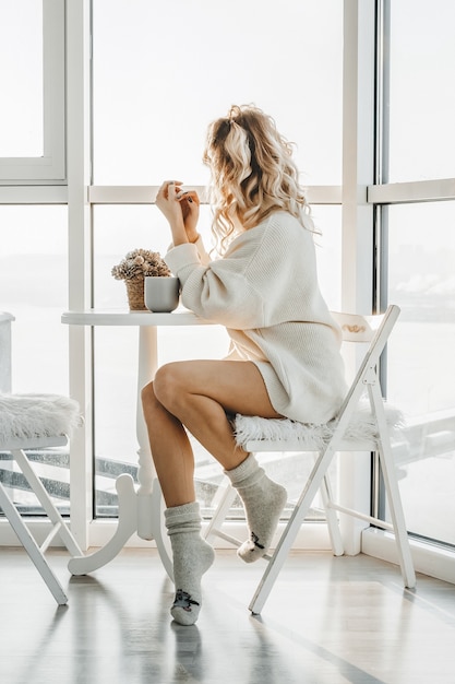 Femme assise près de la fenêtre dans un intérieur festif confortable.