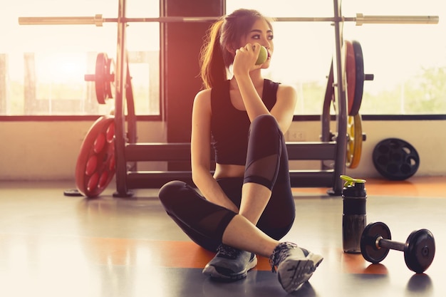 Une femme assise près des haltères dans la salle de sport