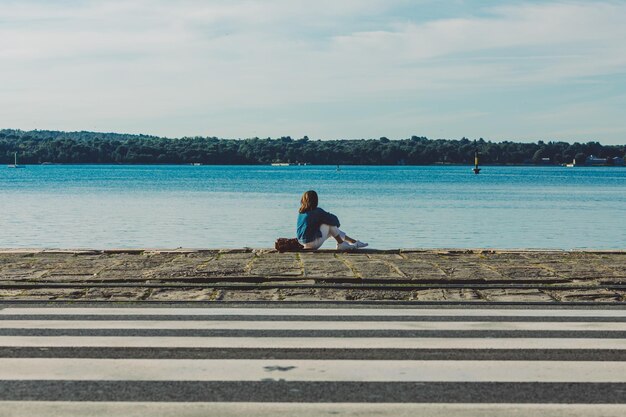 Femme assise à quai regardant la baie de la mer le soir