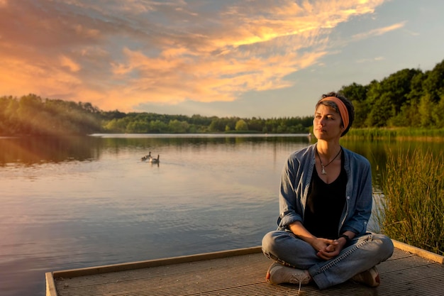 Femme assise et relaxante au bord d'un lac au coucher du soleil