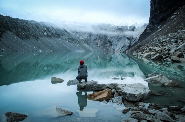 Femme assise sur une roche contre les montagnes dans le lac pendant l'hiver