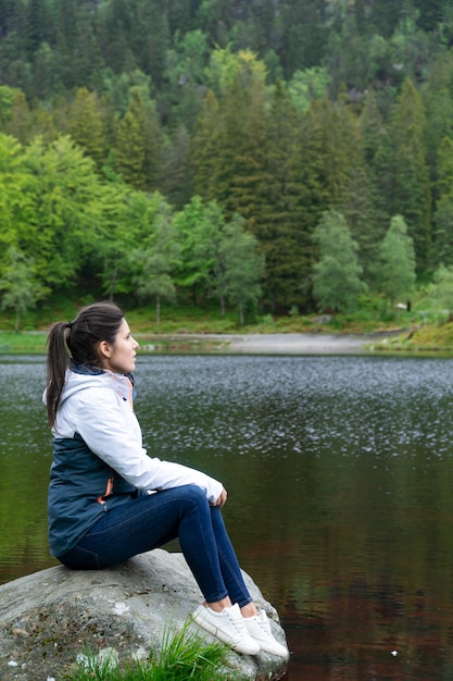 Femme assise sur un rocher contemplant une vue sur le lac et la montagne avec des arbres en arrière-plan