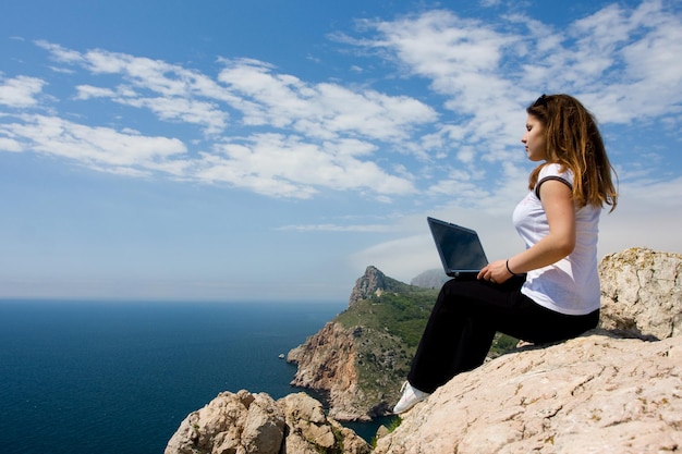 Femme assise sur le rocher avec un ordinateur portable près de la mer