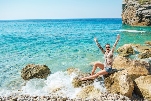 Femme assise sur des rochers à la plage avec les bras vers le haut