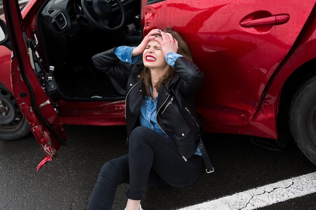 Femme assise sur la route après un accident. Femme blessée se sentant mal après un accident de voiture