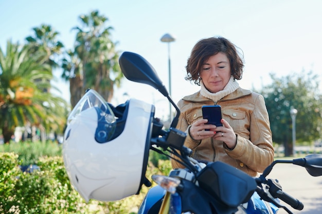 Femme assise sur sa moto garée, consulte son mobile