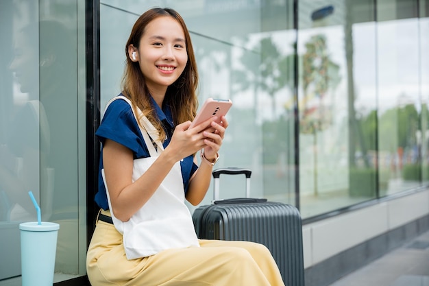 Femme assise avec sa valise à l'aide de son téléphone portable pour envoyer des messages et rester connecté